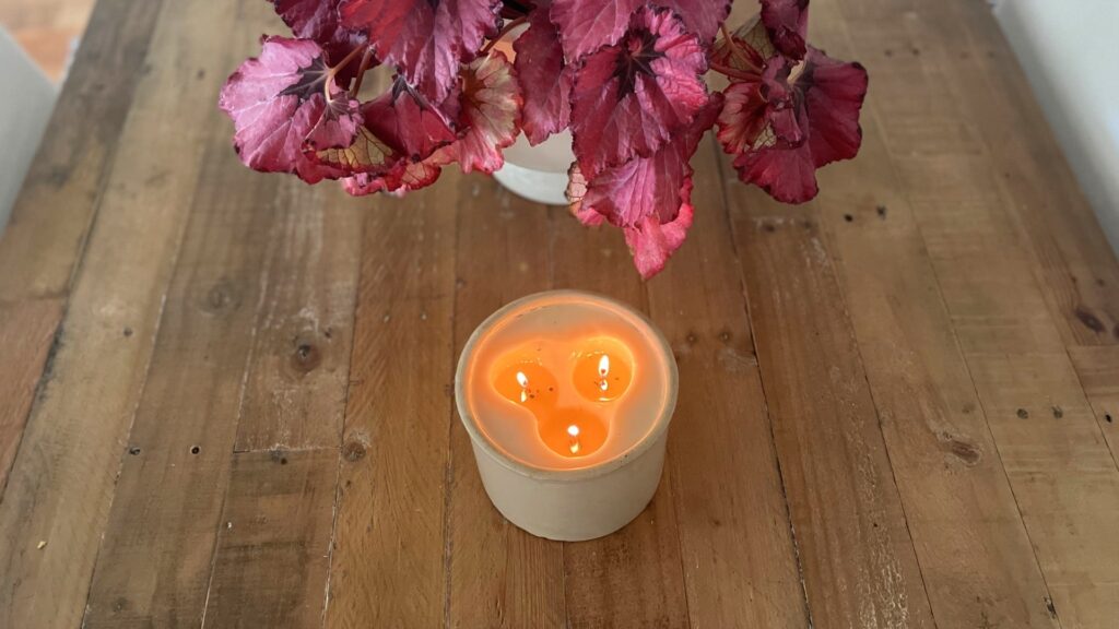 rustic dining table with candle in crock and red begonia plant.