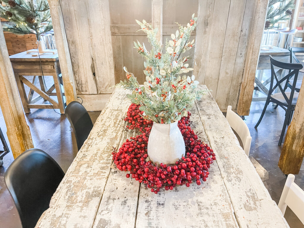 Red berry wreaths around white pitcher of Christmas greens