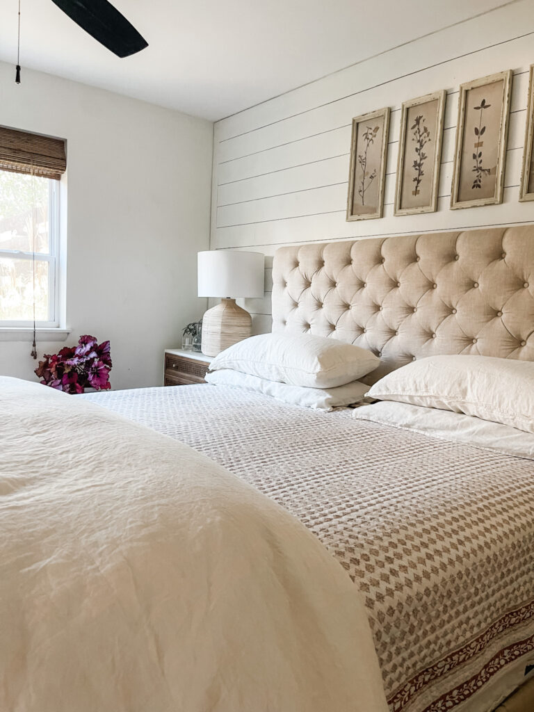 bedroom with shiplap wall, tufted headboard, block print quilt, and down comforter