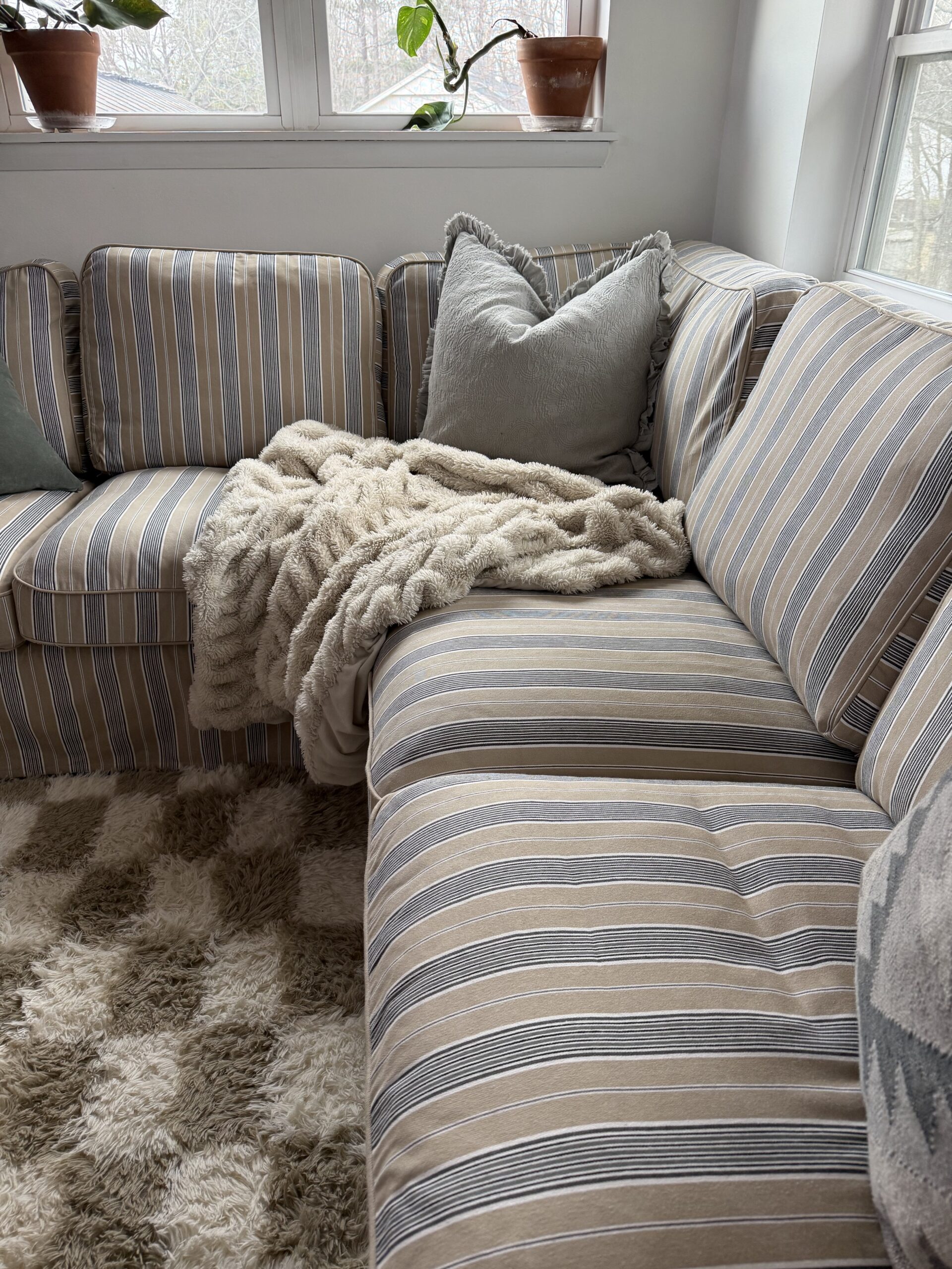 IKEA Uppland sectional with Karlshov Gray Beige slipcover, accessorized with white fur throw, checkered rug, and gray down pillow