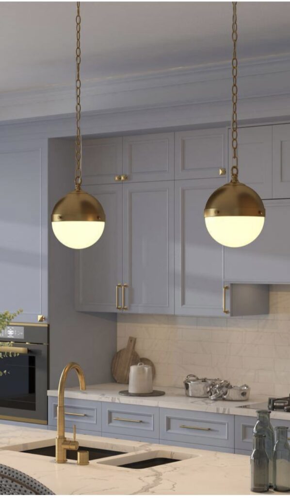 A kitchen with blue gray cabinets and brass handles and kitchen faucet. Brass and milk glass globe pendants with soft light are hanging from brass chain above the kitchen island