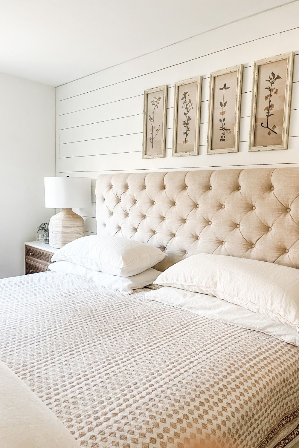 Bedroom with shiplap wall and tufted headboard, white pillows and block print quilt