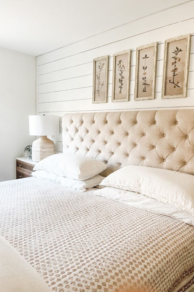 tufted headboard with cream color pillows on bed. Botanical prints above bed