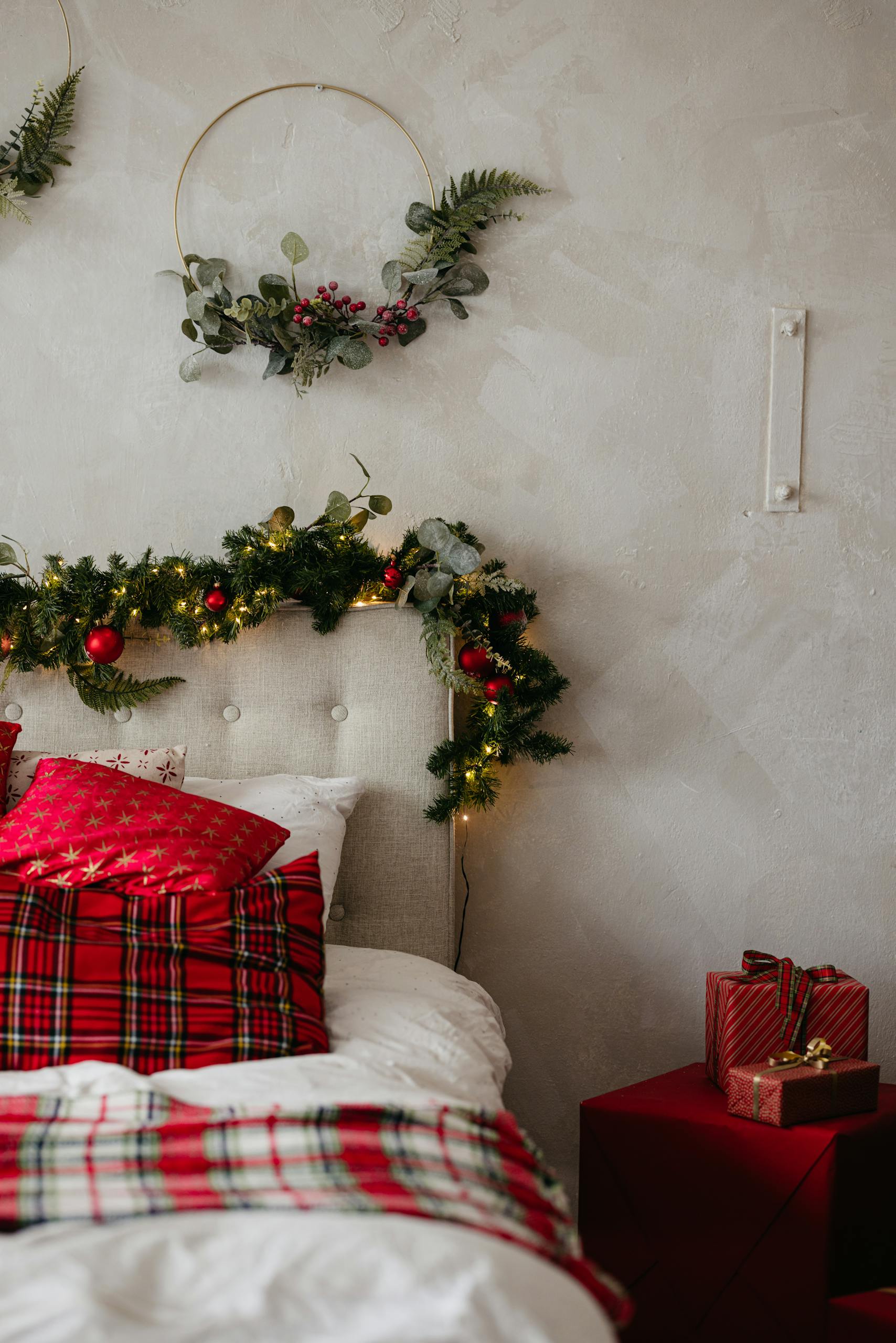Festive holiday bedroom decor with red plaid pillows, garland, and wrapped gifts on a cozy bed.
