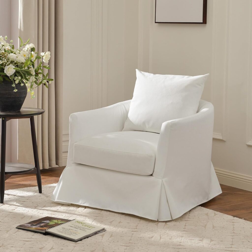 White slipcovered barrel chair in neutral room with wood accent table and flower arrangement